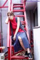 A woman sitting on a red ladder in a red shirt and blue skirt.